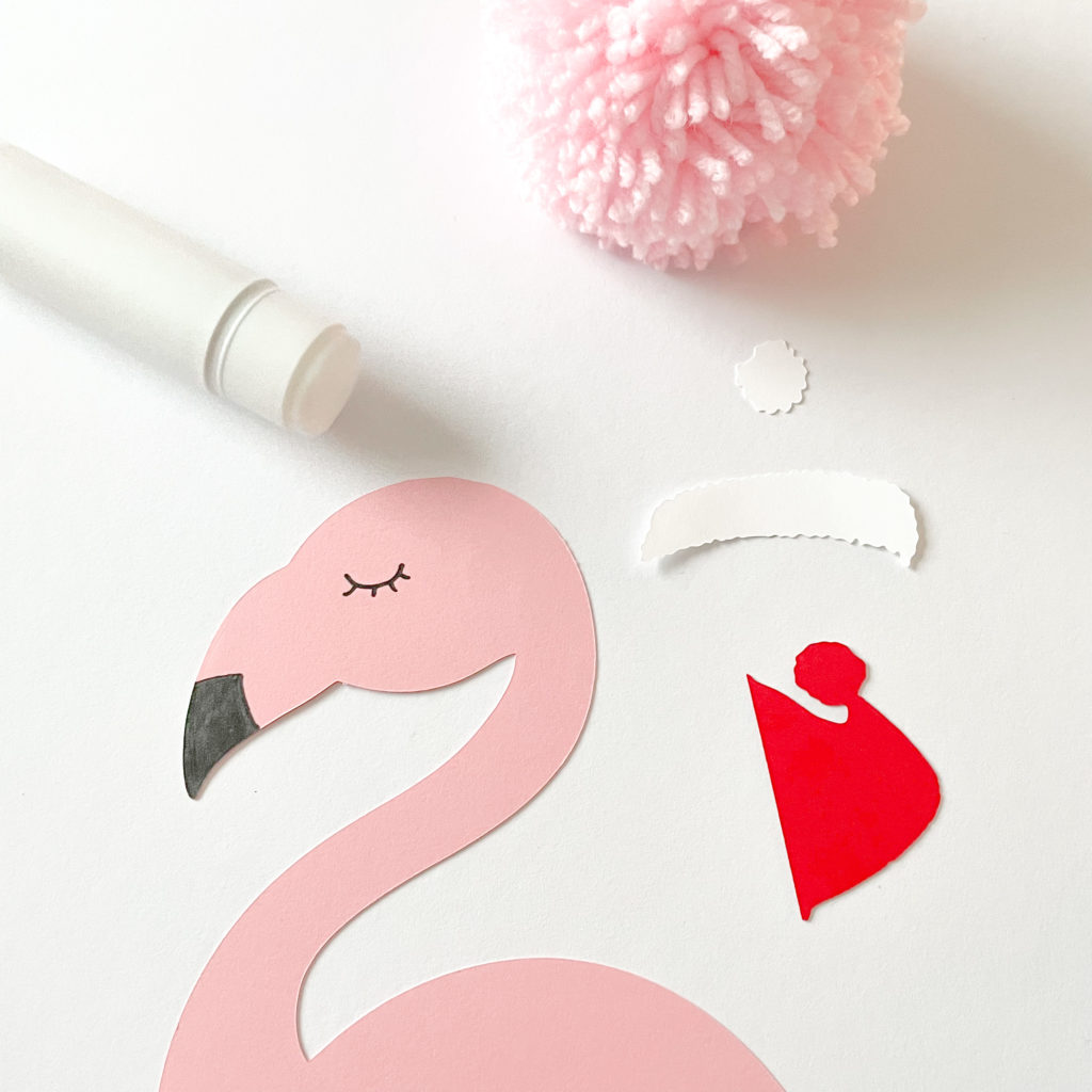Flamant rose en papier avec un pompon rose à côté et un baton de colle