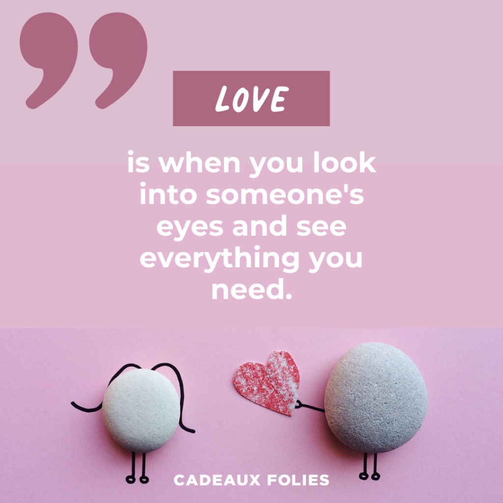 Deux galets avec des jambes et des bras et l'un offre un coeur à l'autre avec la citation "Love is when you look into someone's eyes and see everything you need."