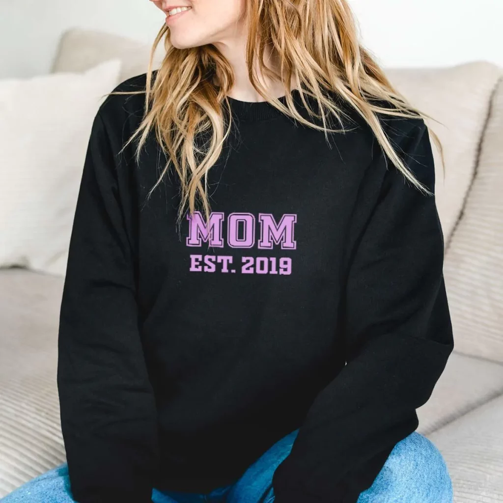 Pull noir en style universitaire avec écriture rose avec écrit Mom est. 2019 