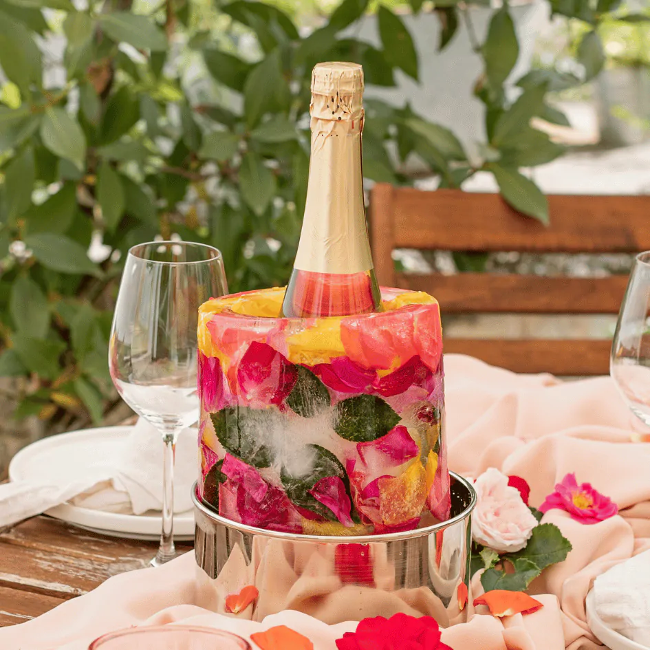 Rafraichisseur de bouteille créatif avec une bouteille de champagne entourée de pétales de rose et de feuilles posés sur une table