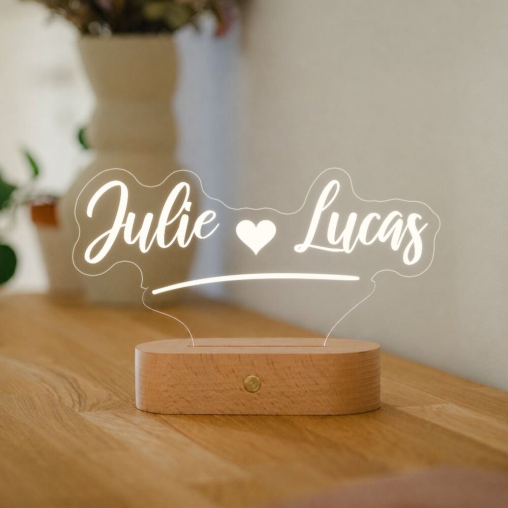 Lampe LED personnalisée avec les prénoms « Julie » et « Lucas » et un cœur, en lumière blanche chaude sur une commode en bois